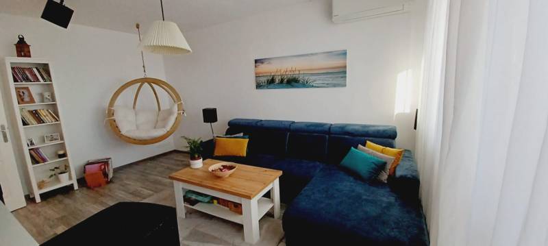 Na predaj 3izbový byt Tranovského , Dúbravka - Obývacia izba s modrou sedačkou, hojdačkou, knihovnicou a podlahou s dreveným dekorom.