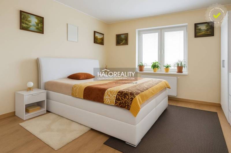 Predaj, rodinný dom Beša - Spálňa v rodinnom dome s posteľou, nočným stolíkom a oknom s izbovými rastlinami.