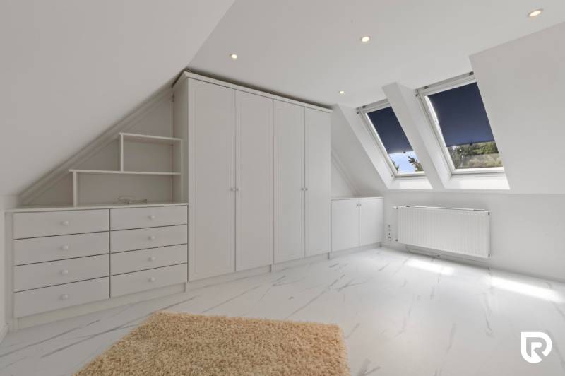 Exkluzívna honosná kúria | 3 ha pozemok | Dunakiliti - HU - Biely interiér so šikmým stropom, skriňou a podlahou s dreveným dekorom.