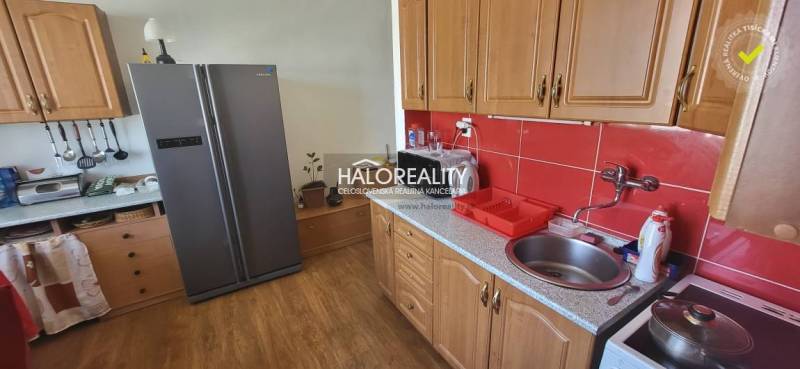 Predaj, jednoizbový byt Žiar nad Hronom, Novomeského - Kuchyňa v 1-izbovom byte s drevenými skrinkami, červenými kachličkami a veľkou chladničkou.