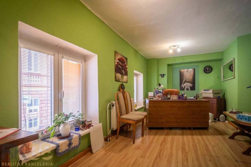 Exkluzívne: Predaj budovy v centre mesta Poprad - Kancelária s dreveným dekorom podlahy, zelené steny, pracovný stôl a dekorácie.
