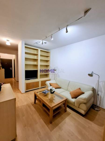 SLNEČNÝ KOMPLETNE ZARIADENÝ 2 IZB. BYT PRI ŠTRKOVECKOM JAZERE.  - Obývacia izba v 2-izbovom byte s krémovou sedačkou a podlahou s dreveným dekorom.