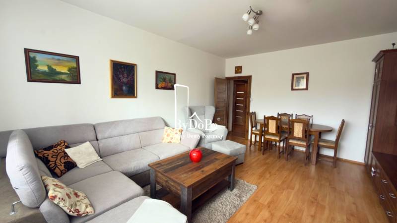 3-izbový zariadený byt, 78 m2, zasklenná loggia, Považská ul., Nitra - Obývačka v 3-izbovom byte s rohovou sedačkou a podlahou s dreveným dekorom.