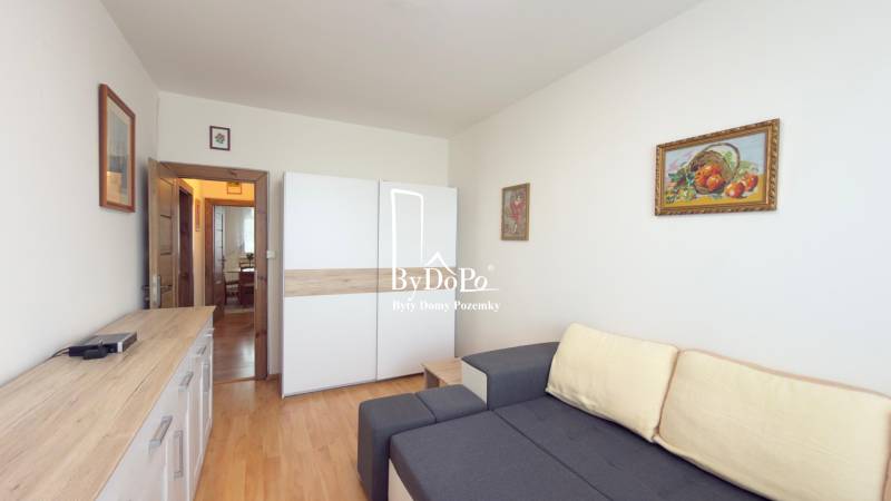 3-izbový zariadený byt, 78 m2, zasklenná loggia, Považská ul., Nitra - Obývacia izba s pohovkou, skriňou a podlahou s dreveným dekorom v 3-izbovom byte.