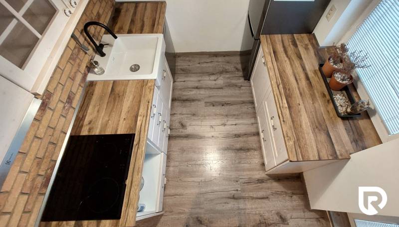 Predaj 3-izb bytu 75 m2 + garáž 18 m2, Trenčín - Pred poľom - Kuchyňa v 3-izbovom byte s podlahou s dreveným dekorom a kuchynskými skrinkami.