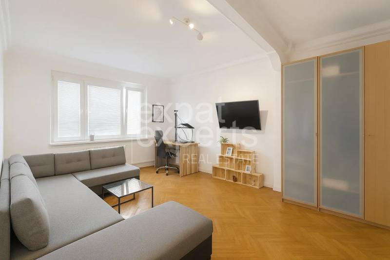 Svetlý, jedinečný 2i byt 62m2, po rekonštrukcií, s pivnicou   - Obývačka v 3-izbovom byte s rohovou sedačkou, pracovným stolom a podlahou s dreveným dekorom.