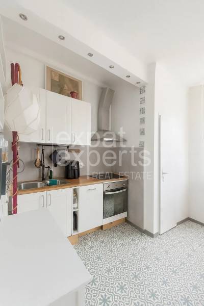 Svetlý, jedinečný 2i byt 62m2, po rekonštrukcií, s pivnicou   - Kuchyňa v 3-izbovom byte s dlažbou, bielymi skrinkami a dreveným dekorom pultu.