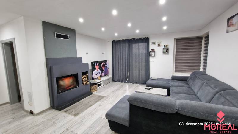 Nový rodinný dom, 7 minút od centra Košíc v tichej uličke pod lesom - Obývačka v rodinnom dome s krbom, šedou sedačkou a televízorom, podlaha s dreveným dekorom.