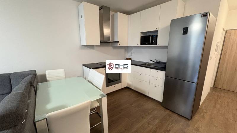 Predaj 1ibyt (garsonka) v uzavretom areáli v DNV (novostavba) - Kuchynská linka v 1-izbovom byte s podlahou s dreveným dekorom a jedálenským stolom.