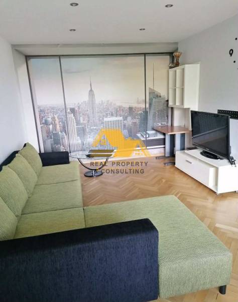 Prenajmem 3 izbový byt v Nových Zámkoch - Obývačka s piškótovým gaučom, tapetou New Yorku a podlahou s dreveným dekorom v 3-izbovom byte.