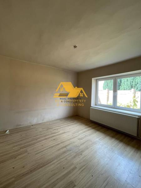 Exkluzívne! Predám rodinný dom v obci Svodín - Izba s podlahou s dreveným dekorom a veľkým oknom v rodinnom dome.