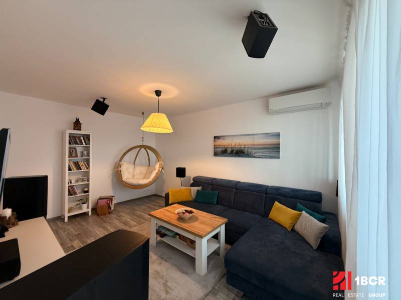 KRÁSNY, ÚTULNÝ A ŠTÝLOVÝ 3 IZBOVÝ BYT | DUBRAVKA - Obývacia izba v 3-izbovom byte s podlahou s dreveným dekorom a závesným kreslom.