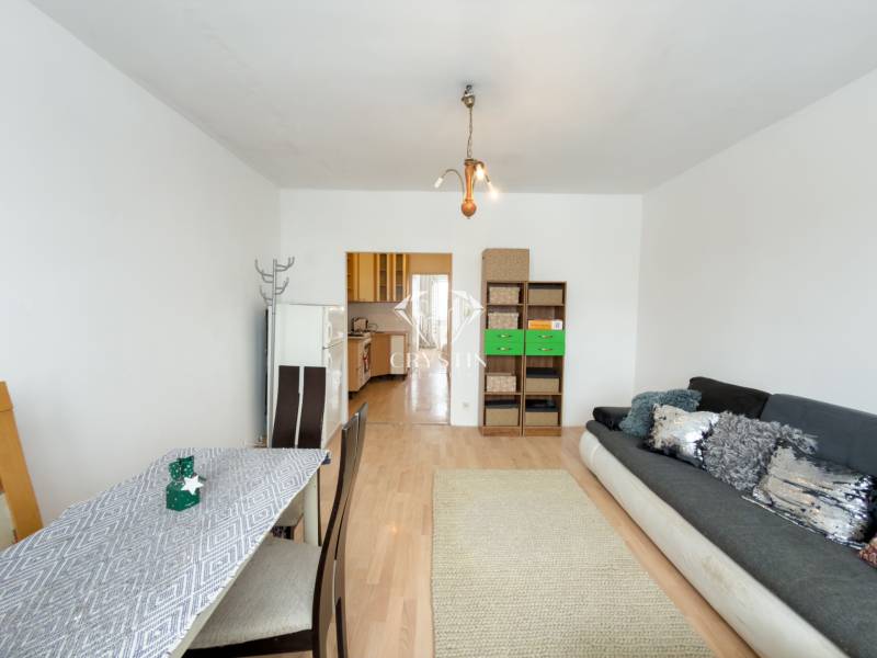 Na predaj 2,5- izbový byt Žilina-Solinky - Obývacia izba v 2-izbovom byte, podlaha s dreveným dekorom, pohovka, jedálenský stôl.