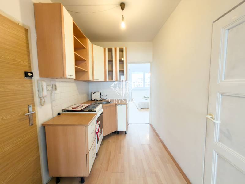 Na predaj 2,5- izbový byt Žilina-Solinky - Kuchyňa v 2-izbovom byte s podlahou s dreveným dekorom a bielymi skrinkami.