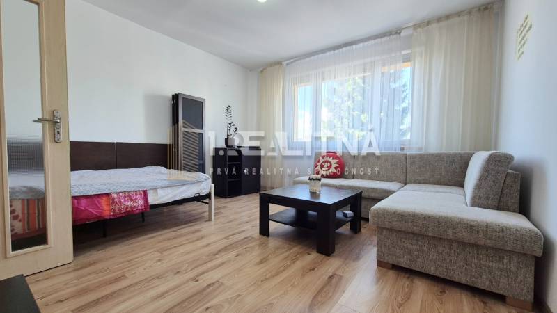 PRIESTRANNÝ 1-IZBOVÝ BYT, 38 M², BANSKÁ BYSTRICA - SITNIANSKA - Obývacia časť 1-izbového bytu s pohovkou, stolíkom a podlahou s dreveným dekorom.
