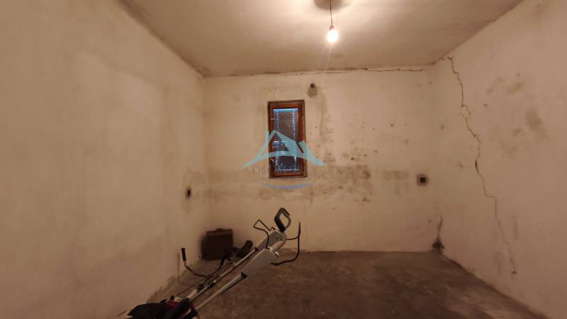 Rodinný dom v obci Čebovce v okrese Veľký Krtíš. - Suterén s oknom v rodinnom dome, steny s prasklinami a jednoduchým osvetlením.