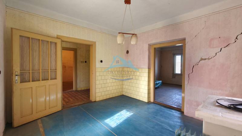 Rodinný dom v obci Čebovce v okrese Veľký Krtíš. - Izba s modrou podlahou s dreveným dekorom, starými dverami a prasklinami v stene.