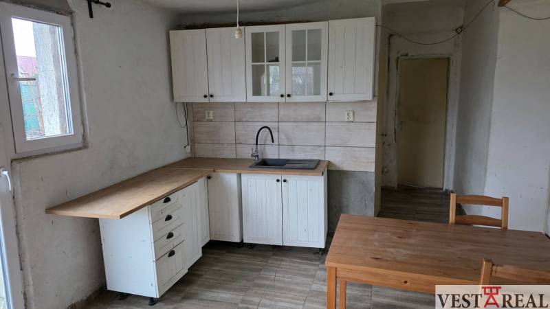 Na predaj 5 izbový rodinný dom Vinohrady nad Váhom - Kuchyňa v rodinnom dome s bielymi skrinkami a podlahou s dreveným dekorom.