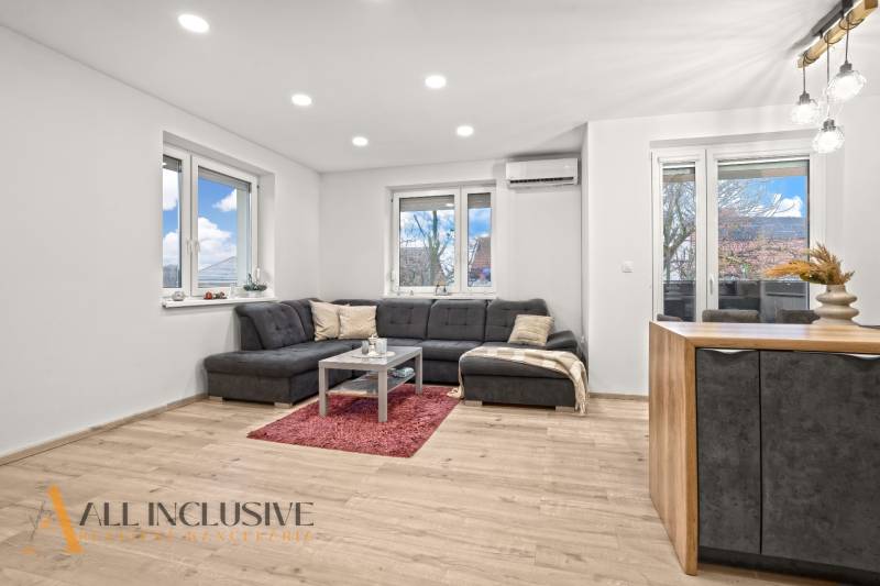 REZERVOVANÉ | NA PREDAJ 3-IZBOVÝ BYT S BALKÓNOM, VRAKÚŇ - Obývačka 3-izbového bytu s podlahou s dreveným dekorom, pohodlným sedením a veľkými oknami.