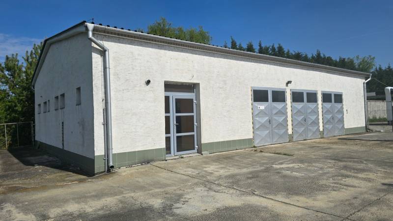 Prenájom haly v Šali – Veča | 220 m² | Ideálne na podnikanie - Biela budova s kovovými dverami v skladovej a halovej zóne mesta Šaľa.