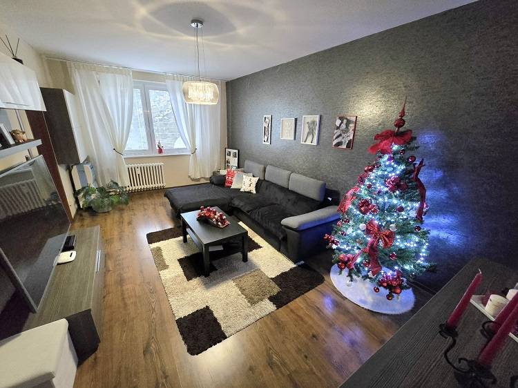 Predaj,trojizbový byt SNP, Holíč - Obývacia izba v 3-izbovom byte s pohovkou, svetelným stromčekom a podlahou s dreveným dekorom.