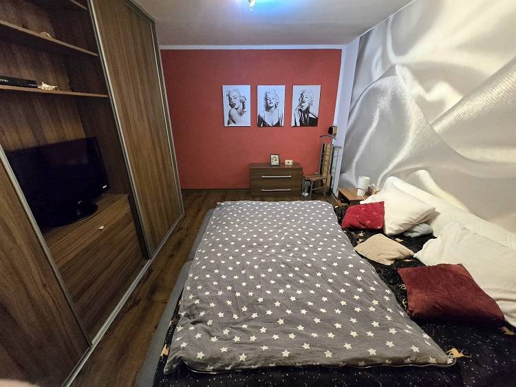 Predaj,trojizbový byt SNP, Holíč - Spálňa v 3-izbovom byte s podlahou s dreveným dekorom, červenou stenou a umeleckými portrétmi.