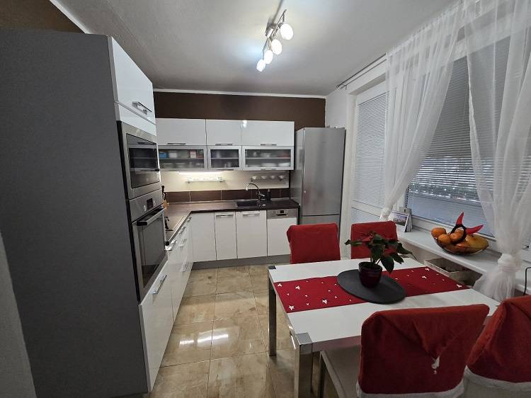 Predaj,trojizbový byt SNP, Holíč - Kuchyňa v 3-izbovom byte s lesklými bielymi skrinkami, spotrebičmi a jedálenským stolom.