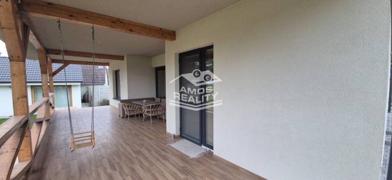 Na predaj 4 izbový RD v obci  Studienka, garáž, sauna, pozemok 719 m2 - Terasa rodinného domu v Studienke s hojdacou hojdačkou a nábytkom, podlaha s dreveným dekorom.