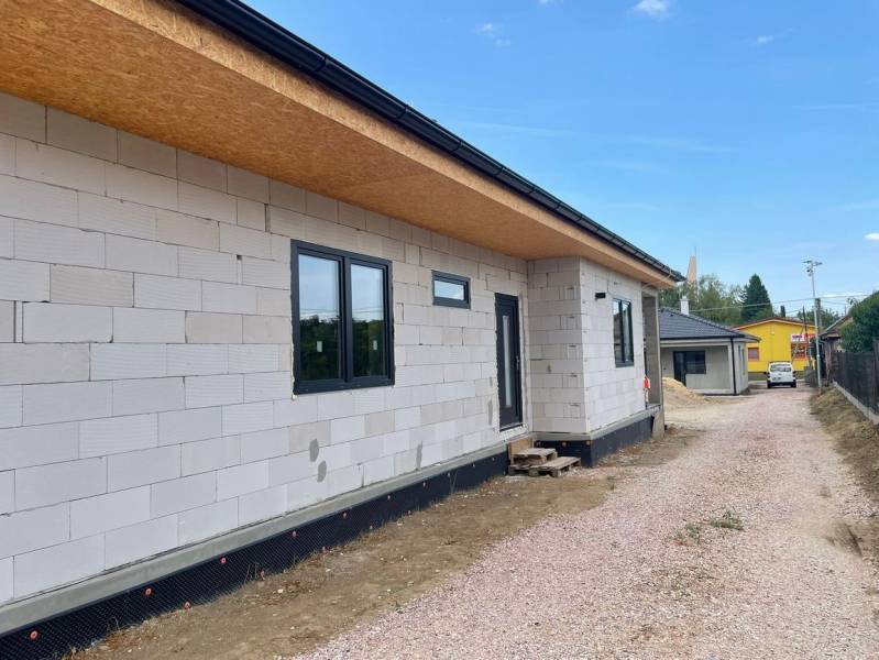 Ponúkame na predaj štvorizbový rodinný dom v obci Radava. - Rodinný dom v Radave počas výstavby s nezateplenou fasádou a štrkovou cestou.