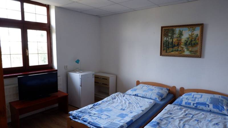 Ponúkame na predaj penzión v Poľnom Kesove - Izba s dvoma posteľami, televízorom, chladničkou a obrazom, podlaha s dreveným dekorom.