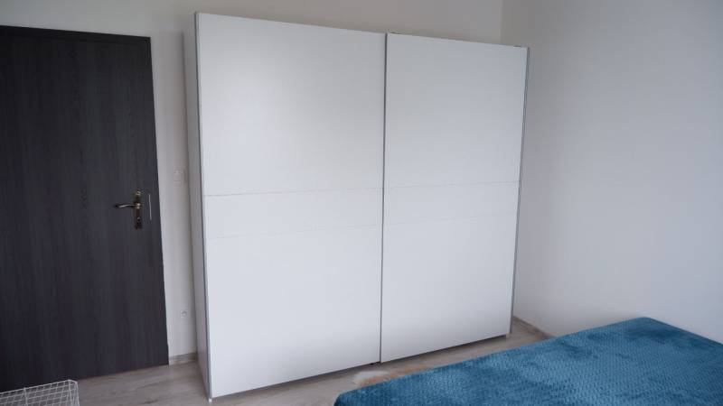 Ponúkame na predaj 3 izbový radový dom v obci Rastislavice. - Biela skriňa a posteľ s modrou prikrývkou v interiéri rodinného domu.