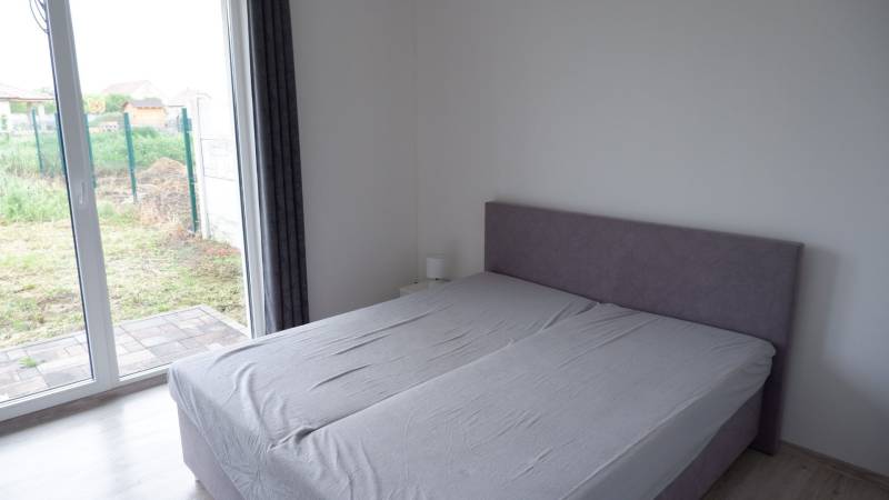 Ponúkame na predaj 3 izbový radový dom v obci Rastislavice. - Spálňa v rodinnom dome s posteľou a veľkými oknami na podlahu s dreveným dekorom.