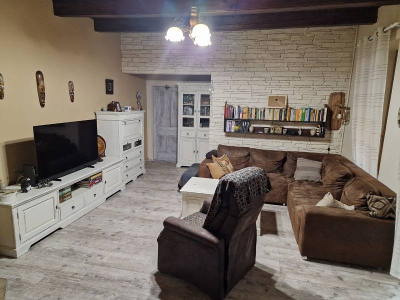 Krásny rodinný dom s rozľahlým pozemkom - Obývacia izba s rohovou sedačkou, bielym nábytkom a podlahou s dreveným dekorom v rodinnom dome.