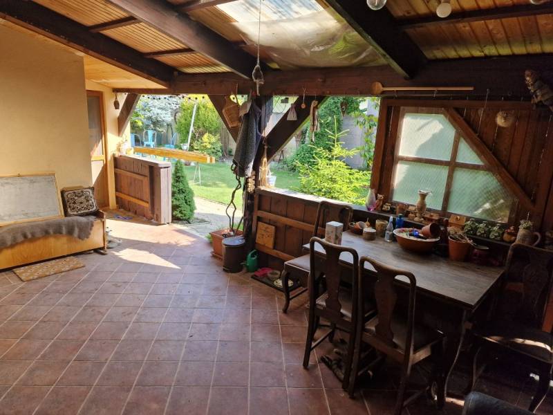 Krásny rodinný dom s rozľahlým pozemkom - Rustikálna terasa rodinného domu s dreveným nábytkom a výhľadom na záhradu.