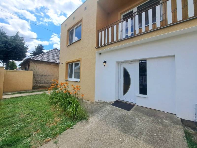 Exkluzívne na predaj 5 izbový rodinný dom - Rodinný dom vo Veľkej Mači s oranžovými kvetmi, zeleným trávnikom a vstupnými dverami.