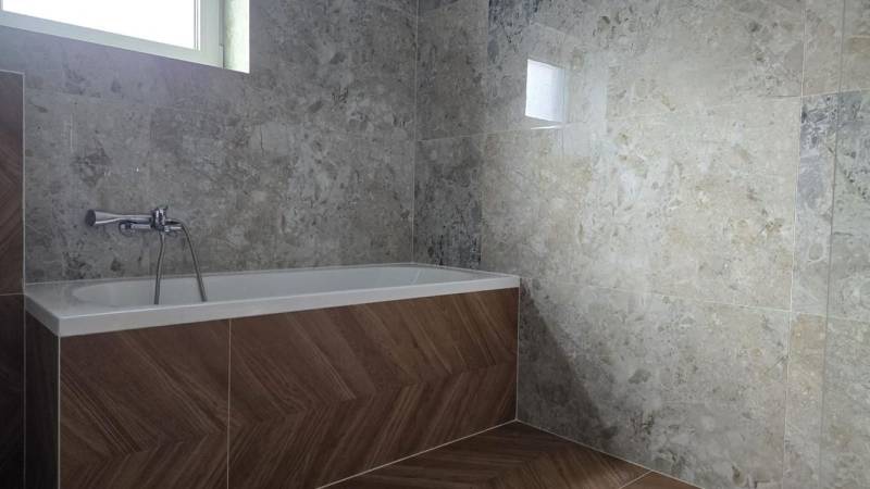 Moderný nízkoenergetický 4-izbový rodinný dom, Cífer – Karlov Dvor - Kúpeľňa v rodinnom dome s vaňou, obklady s kamenným vzorom, podlaha s dreveným dekorom.