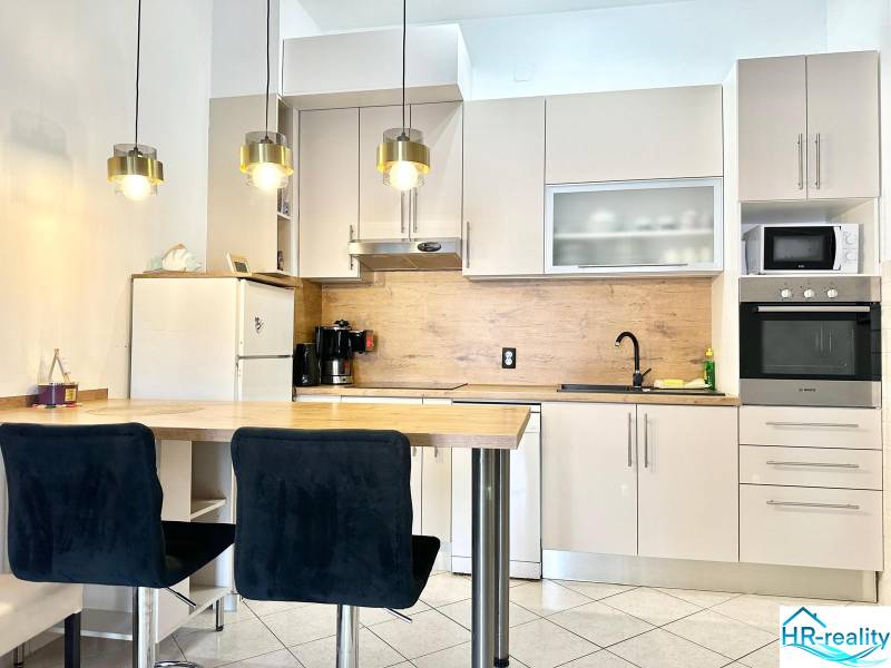 Trogir, Čiovo – pekný, zariadený apartmán len 150m od pláže - Kuchyňa v rekreačnom apartmáne s barovým pultom, závesnými svietidlami a bielou skríňou.