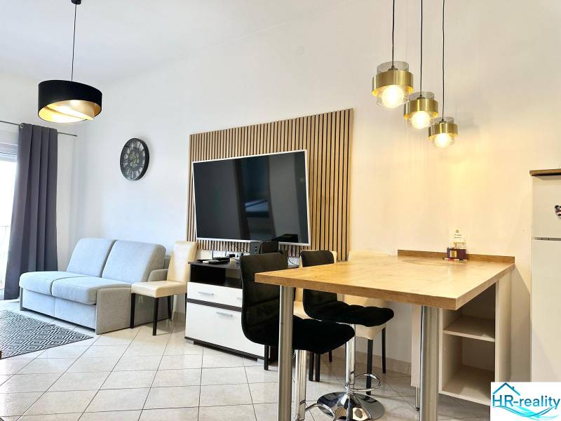 Trogir, Čiovo – pekný, zariadený apartmán len 150m od pláže - Obývacia izba rekreačného apartmánu s televízorom, sedačkou a barovým sedením.