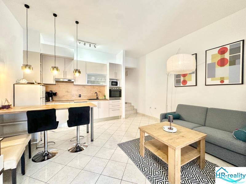 Trogir, Čiovo – pekný, zariadený apartmán len 150m od pláže - Rekreačný apartmán s kuchynským kútom, jedálenským stolom, sedačkou a umeleckými obrazmi na stene.