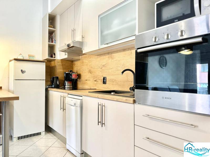 Trogir, Čiovo – pekný, zariadený apartmán len 150m od pláže - Kuchyňa v Rekreačnom apartmáne s bielym nábytkom a dreveným dekorom na stene.