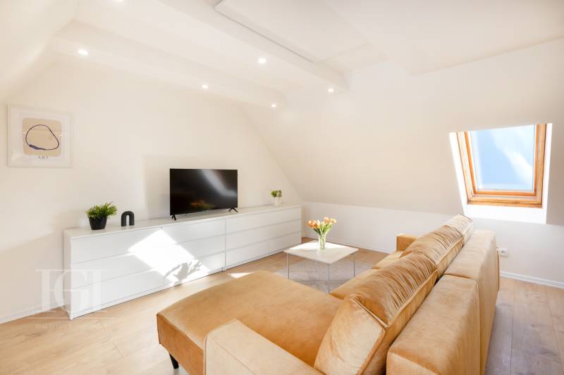  REZERVOVANY-PRENAJOM | NOVÝ 2 i. podkrovný byt v novostavbe - Obývacia izba v 2-izbovom byte s pohovkou, televízorom a strešným oknom, biela komoda.