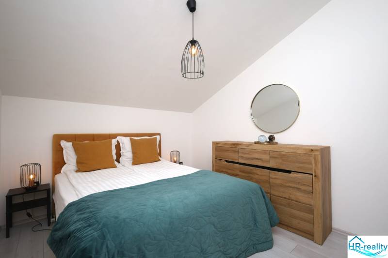 Vodice – novo zrekonštruovaný dvojspálňový apartmán s výhľadom na more - Spálňa v rekreačnom apartmáne s posteľou, drevenou komodou, zrkadlom a lampou.