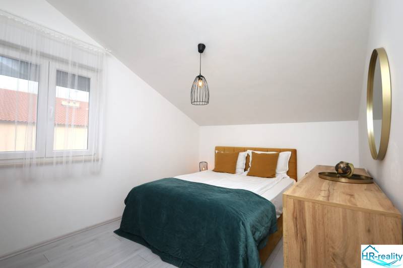 Vodice – novo zrekonštruovaný dvojspálňový apartmán s výhľadom na more - Spálňa v Rekreačnom apartmáne s manželskou posteľou, oknom a komodou pod šikmou strechou.