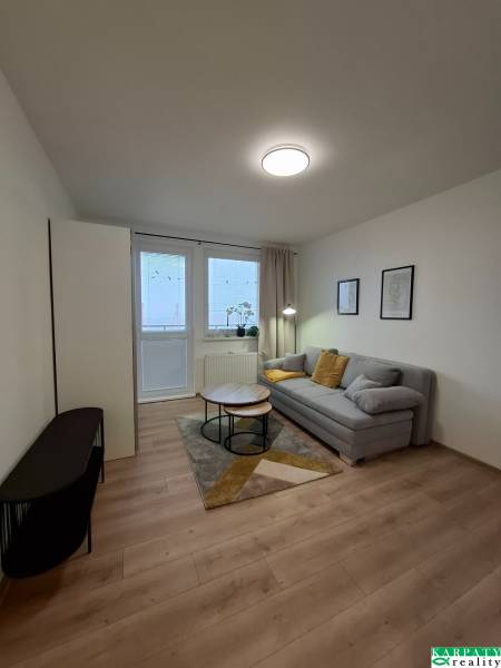 Zrekonštruovaná   garsónka s balkónom na Spartakovskej ulici v Trnave - Garsónka s pohovkou, konferenčným stolíkom a podlahou s dreveným dekorom.