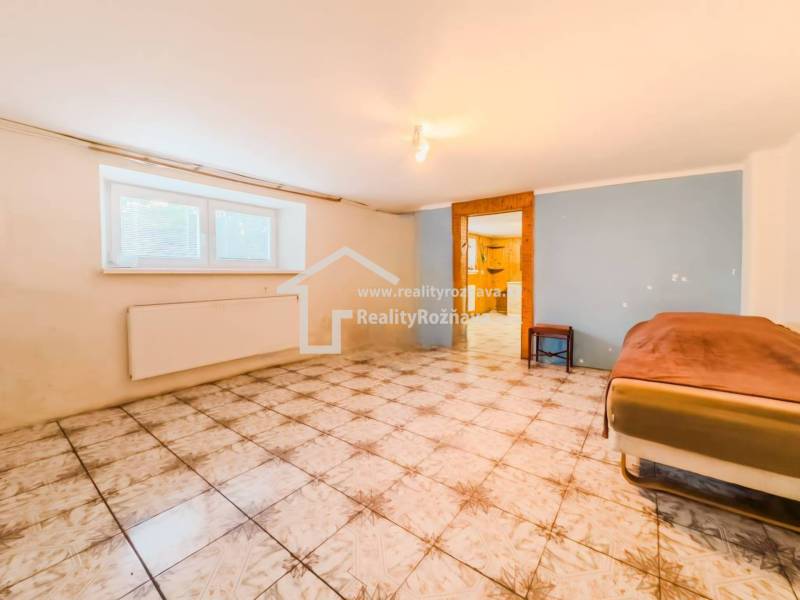 Rodinný dom vo vyhľadávanej obci Betliar. - Izba s dlažbou v rodinnom dome, posteľ pri stene, okno s radiátorom.