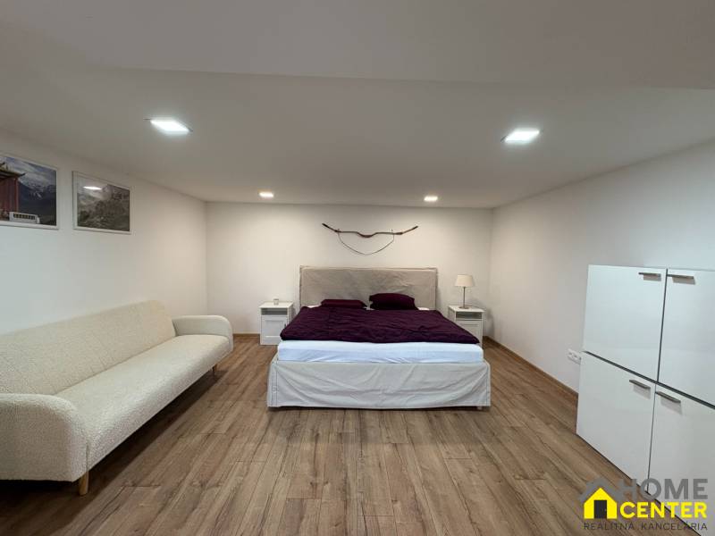 NA PRENÁJOM krásny 1 izbový apartmán so záhradou v srdci Komárna - Interiér 1-izbového bytu s posteľou, pohovkou a podlahou s dreveným dekorom.