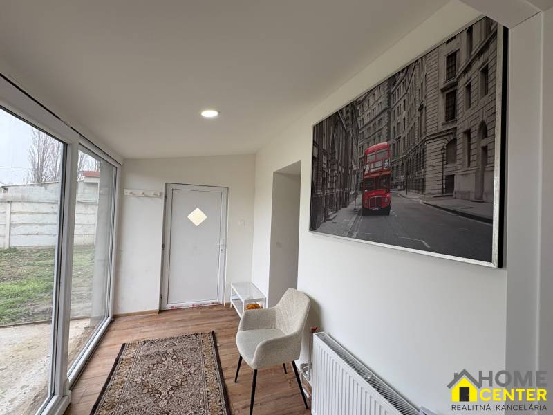 NA PRENÁJOM krásny 1 izbový apartmán so záhradou v srdci Komárna - Interiér 1-izbového bytu s podlahou s dreveným dekorom, sklenenými dverami a umením na stene.