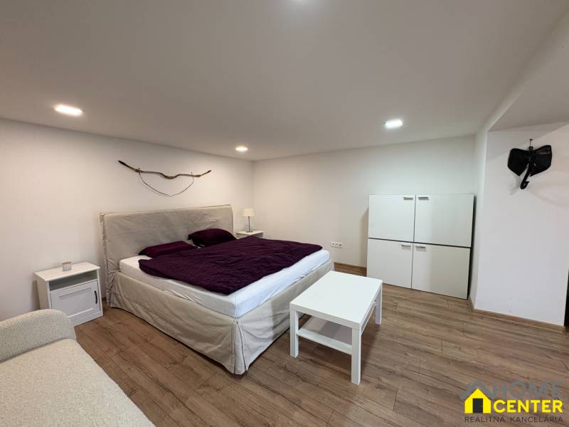 NA PRENÁJOM krásny 1 izbový apartmán so záhradou v srdci Komárna - Spálňa v 1-izbovom byte s podlahou s dreveným dekorom a posteľou s fialovým prehozom.