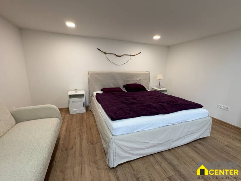 NA PRENÁJOM krásny 1 izbový apartmán so záhradou v srdci Komárna - Spálňa v 1-izbovom byte s podlahou s dreveným dekorom, posteľou a dekorativným prvkom na stene.