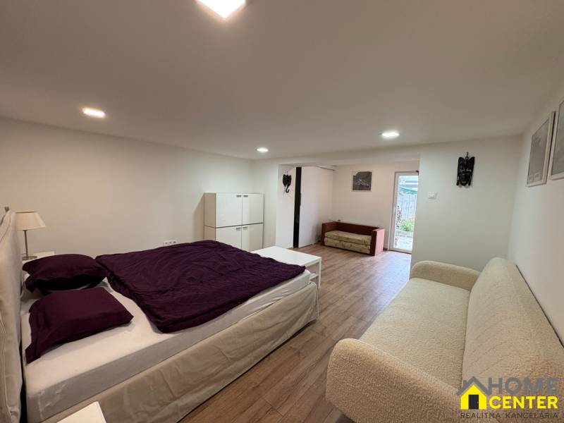 NA PRENÁJOM krásny 1 izbový apartmán so záhradou v srdci Komárna - Spálňa v 1-izbovom byte s podlahou s dreveným dekorom, jednoduchý nábytok a dekorácie.